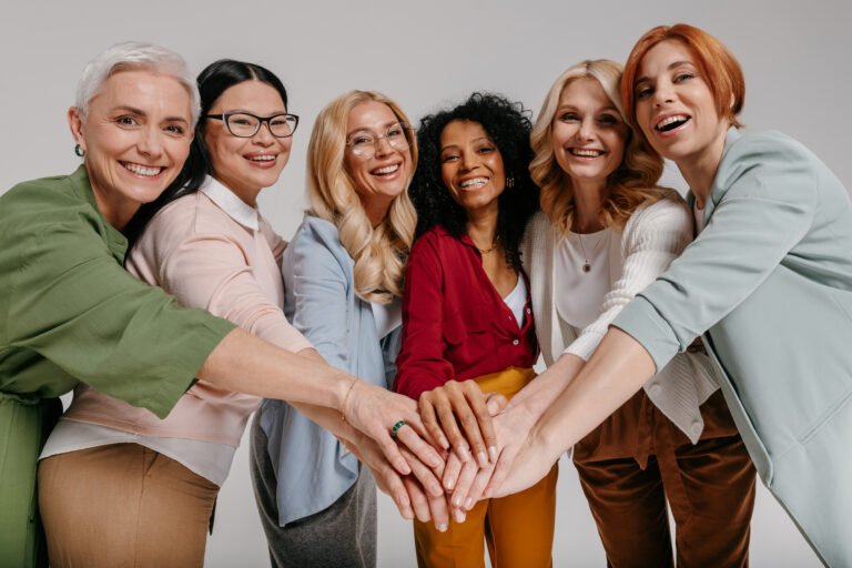 Multi-ethnic group of happy mature women holding hands together against grey background